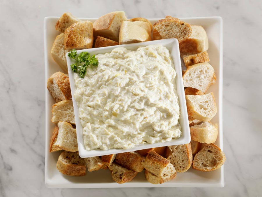 A platter with crackers and a bowl of artichoke dip.