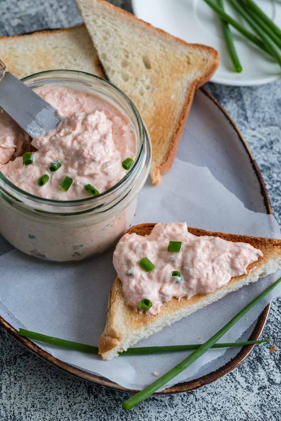 A glass jar filled with salmon cream cheese dip with slices of bread on the side.