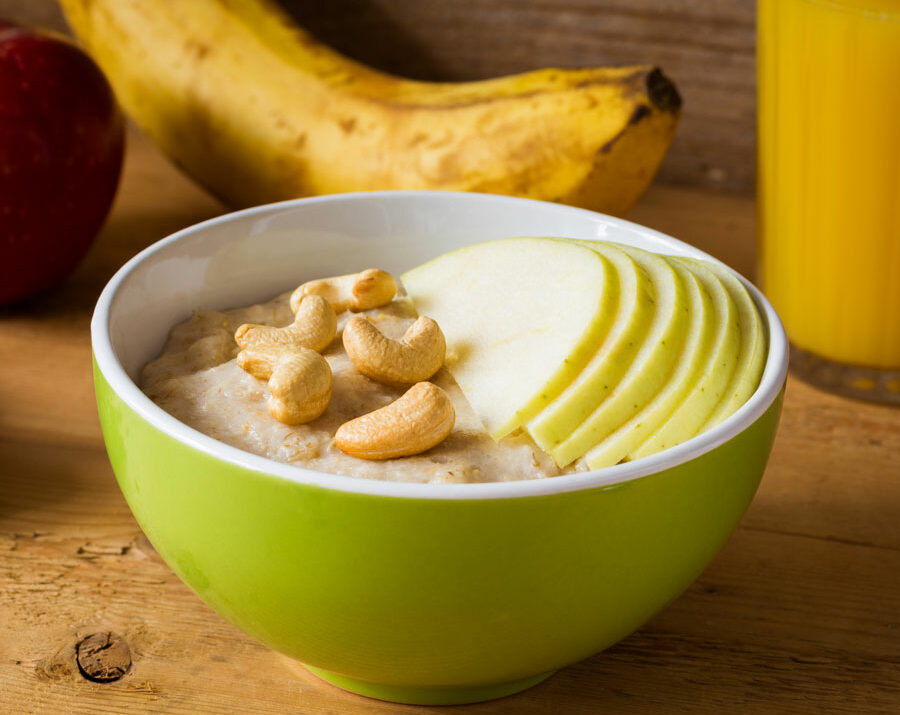 A bowl of oatmeal topped with cashews and apples