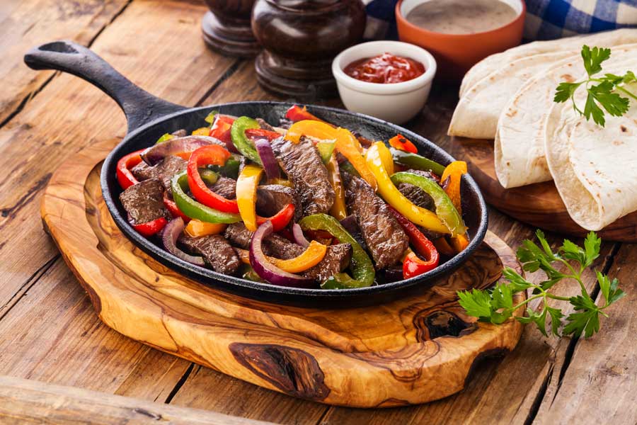 A cast iron skillet with steak fajitas and peppers.