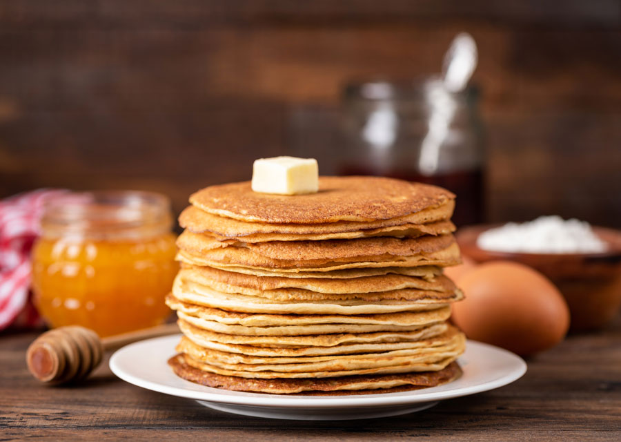 Buckwheat pancakes on a white plate with honey in the background