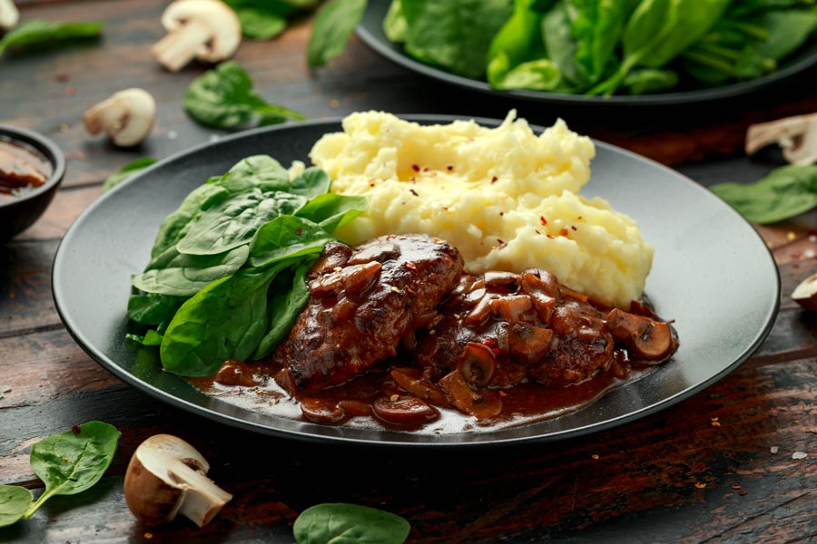 Cube steak on a plate with gravy, mashed potatoes and greens.