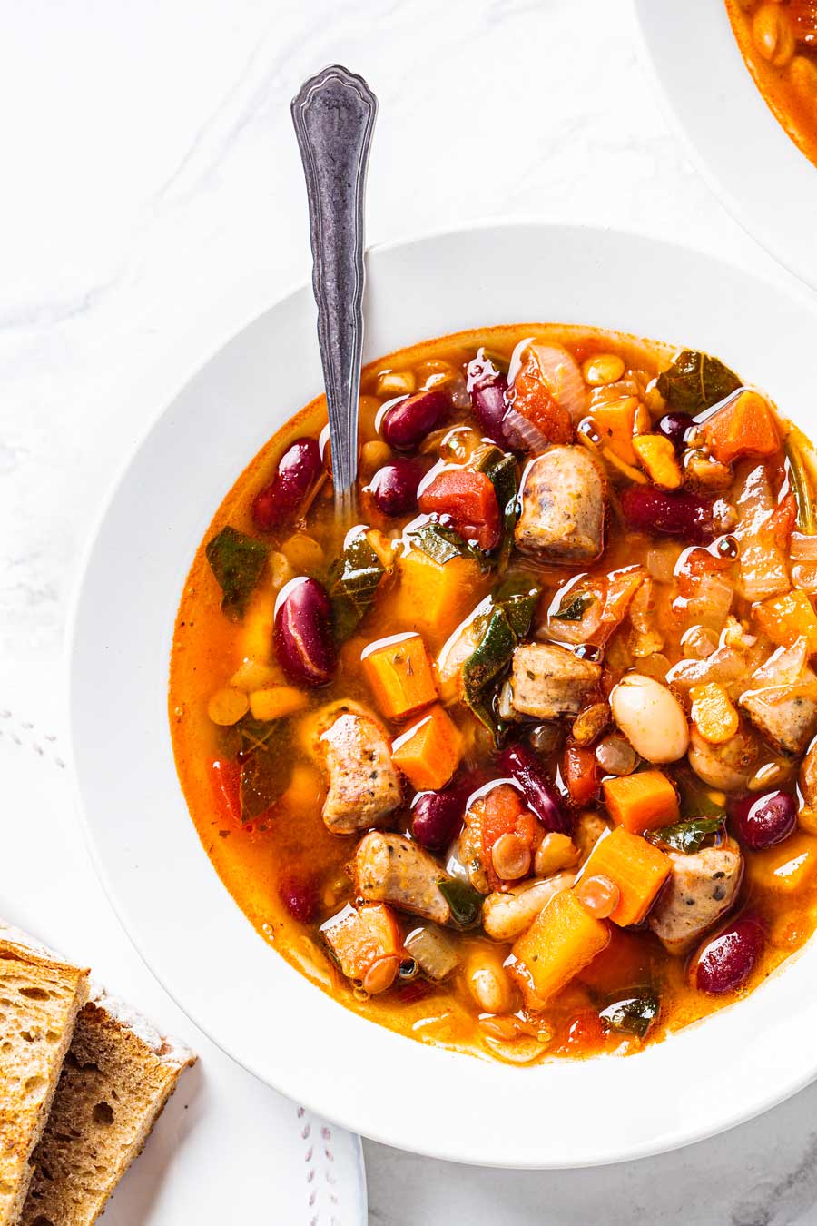 Sweet Potato Minestrone soup in a white bowl with a spoon.