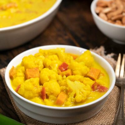 A white bowl filled with spiced cauliflower in a coconut-turmeric spiced sauce.