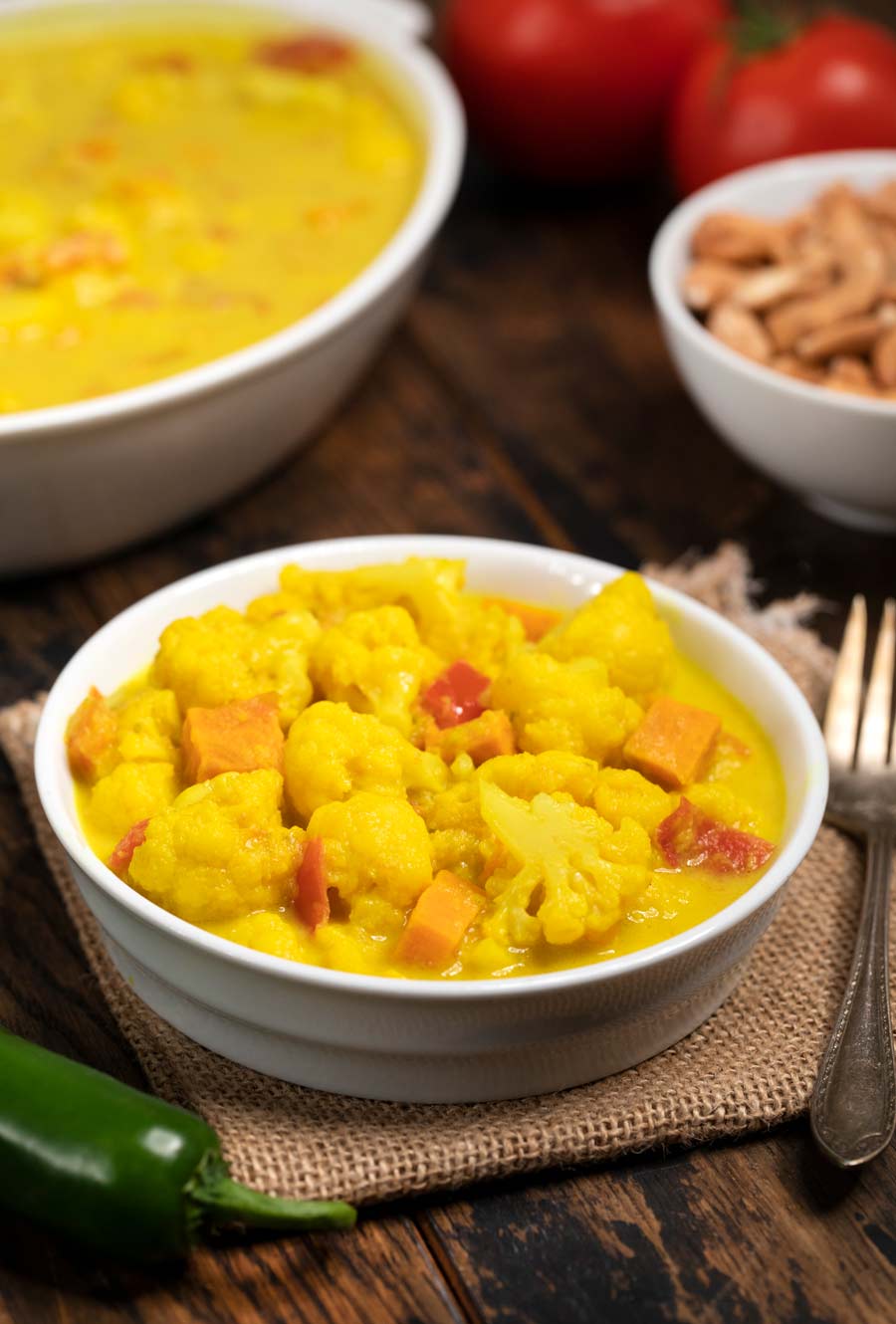 A white bowl filled with spiced cauliflower in a coconut-turmeric spiced sauce.