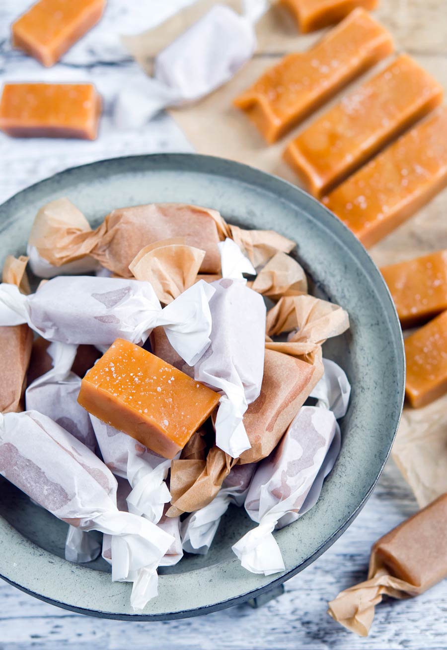 An overhead shot of a bowl of homemade caramel candies covered in wax paper.