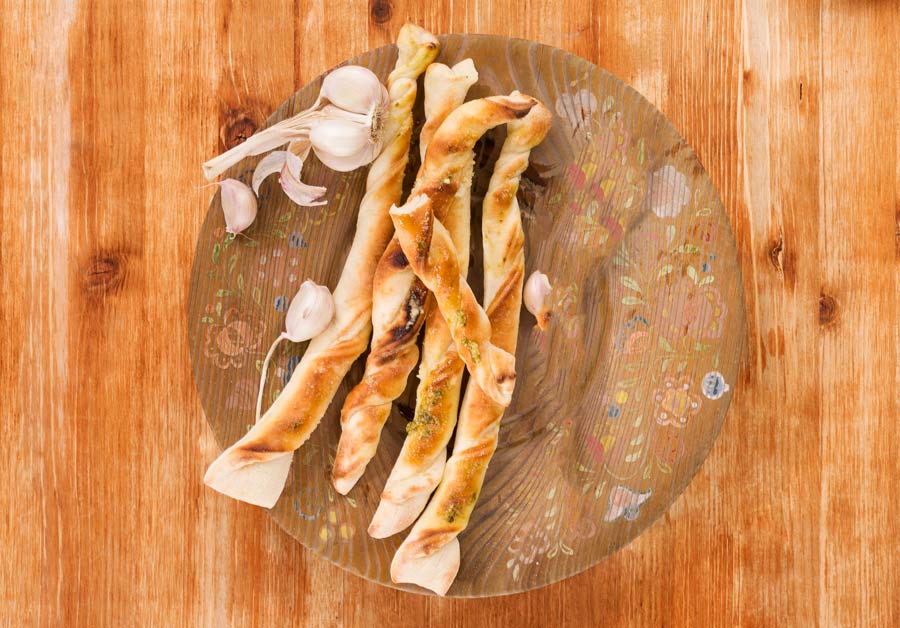 Breadsticks with garlic on wooden plate on wooden background, top view. Culinary pizzastick eating, rustic styles.
