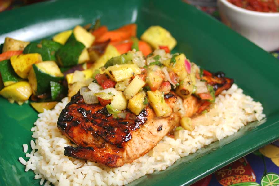 A green plate with white rice, topped with a piece of salmon and pineapple salsa.