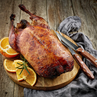 A grilled duck on a cutting board with orange slices on the side.