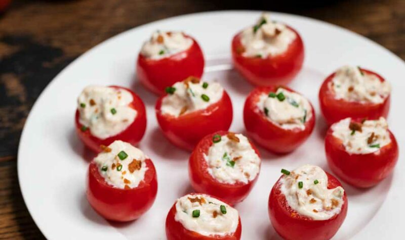 A white plate with cherry tomatoes filled with bacon, cream cheese, sour cream and chives.