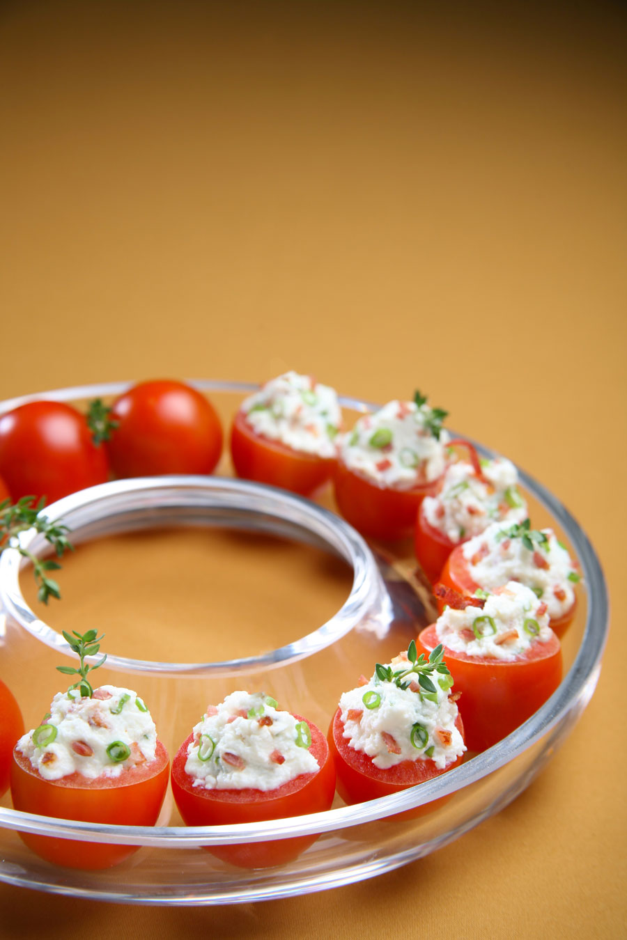 A circular plate filled with cherry tomatoes stuffed with cream cheese and topped with chives and bacon