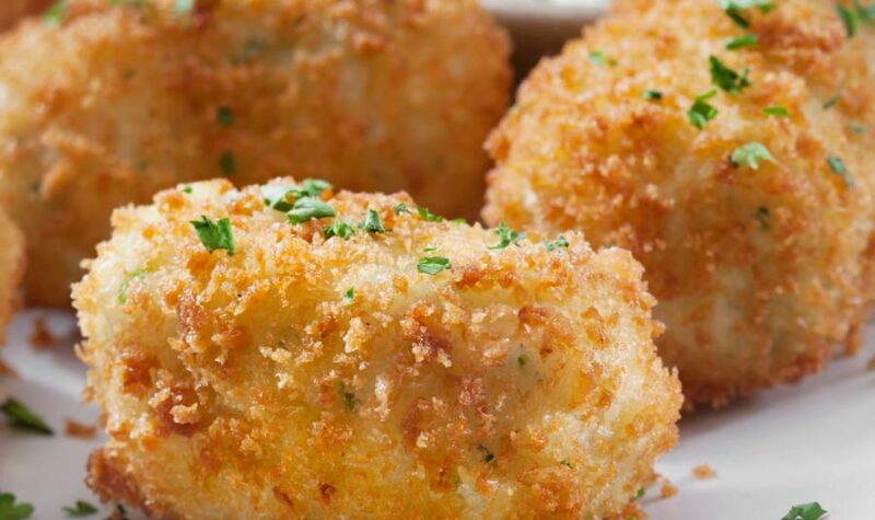 Fried mashed potato balls sprinkled with chives and a sauce on the side