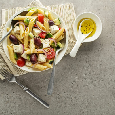 Greek pasta salad in a bowl with herbed olive oil on the side.