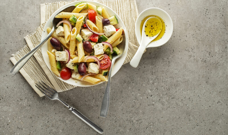 Greek pasta salad in a bowl with herbed olive oil on the side.