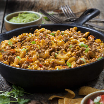A skillet filled with taco pasta salad with corn chips on the side