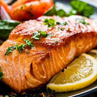 Baked salmon with parsley on top and a lemon wedge on the side.