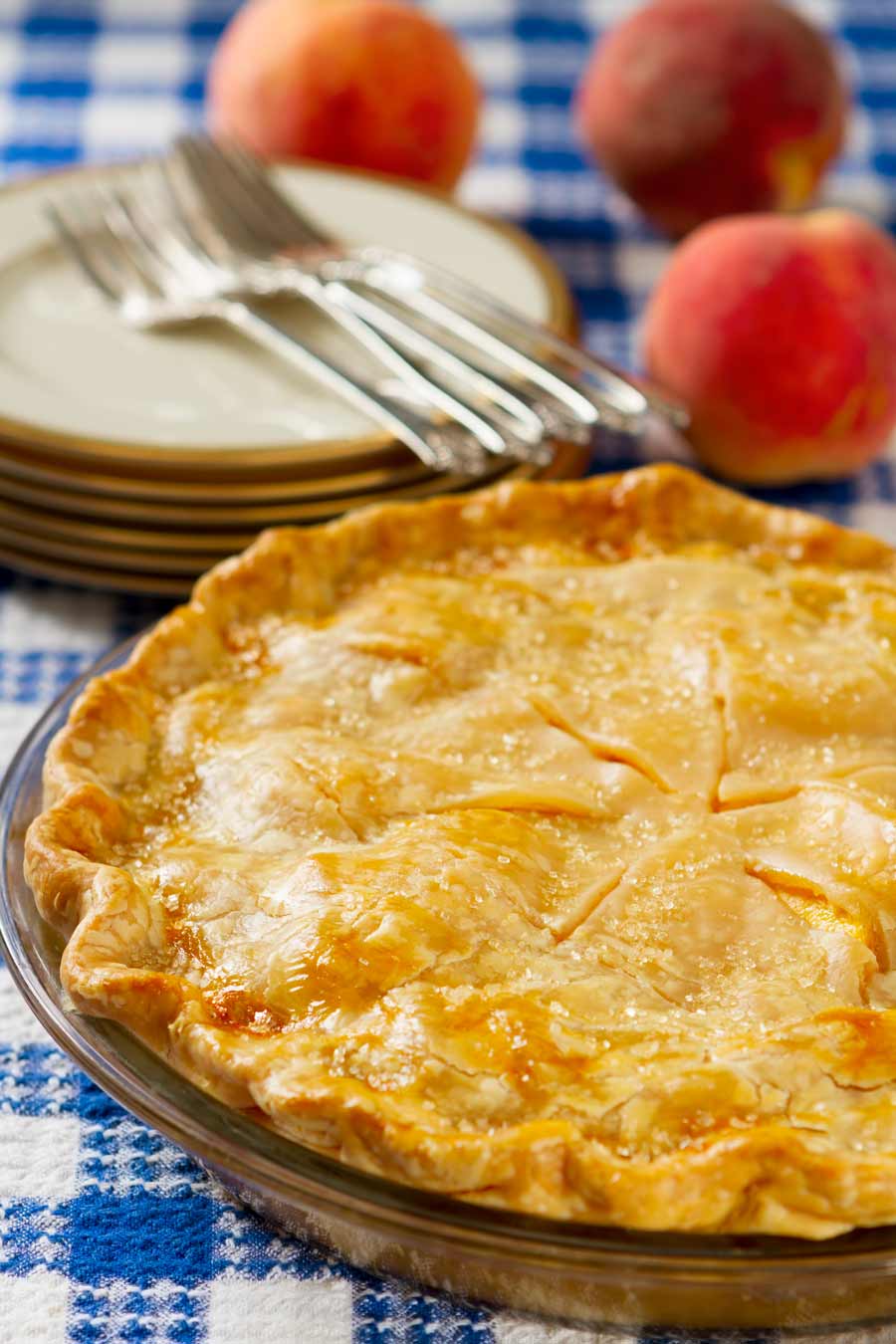 A strawberry peach pie with peaches in the background