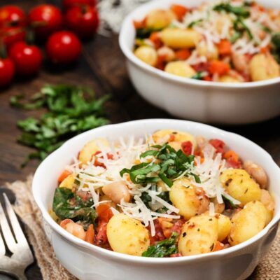 White Bean Gnocchi Skillet with tomatoes and vegan parmesan and basil on the side.
