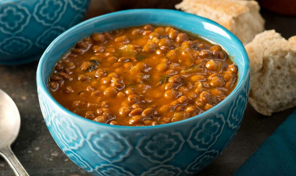 A bowl of lentil soup with veggies, and bread on the side