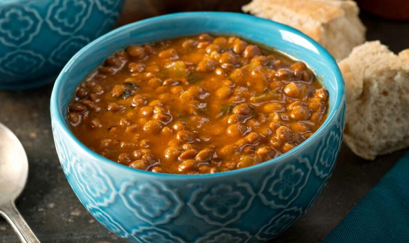 A bowl of lentil soup with veggies, and bread on the side